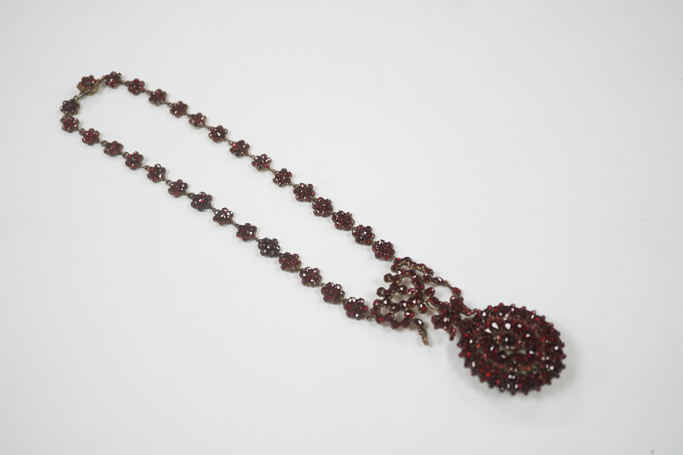 A Victorian gilt metal and facet cut garnet cluster set mourning drop pendant necklace, overall 50cm.